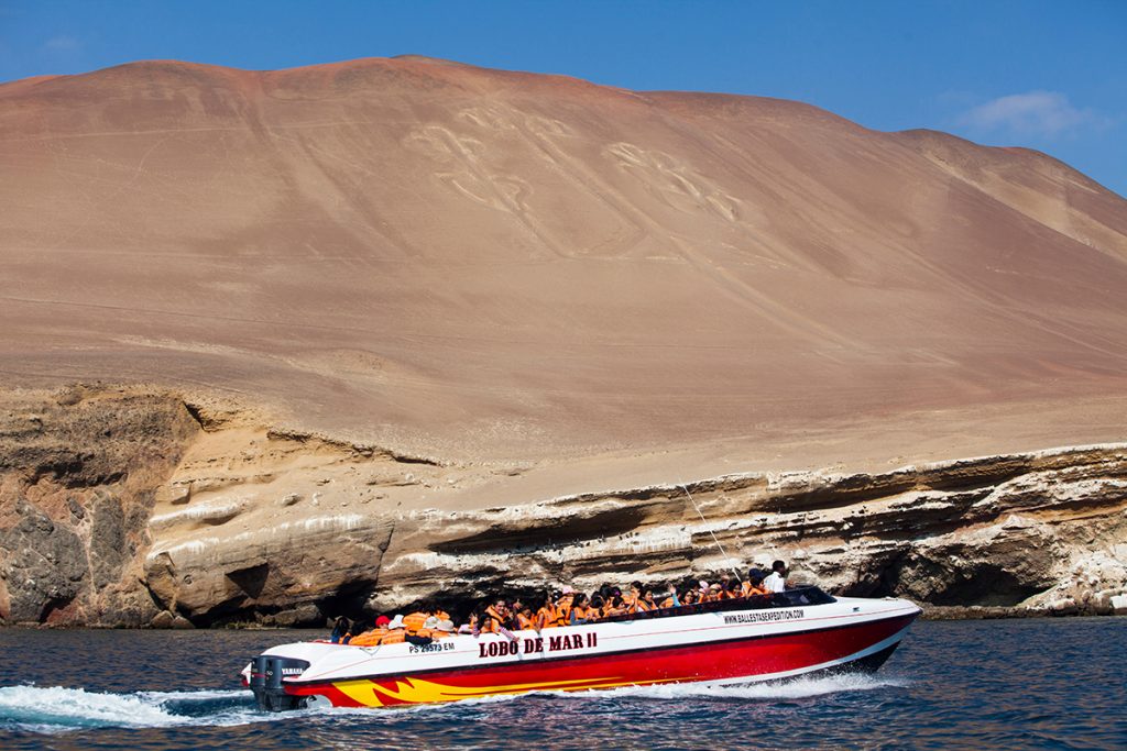 Touristen fahren in einem Boot am Kandelaber in Paracas vorbei