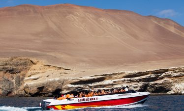 Touristen fahren in einem Boot am Kandelaber in Paracas vorbei