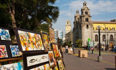 Im Parque Central in Miraflores, Lima, werden Bilder verkauft. Im Hintergrund ist die Kirche "Virgen Milagrosa" zu sehen
