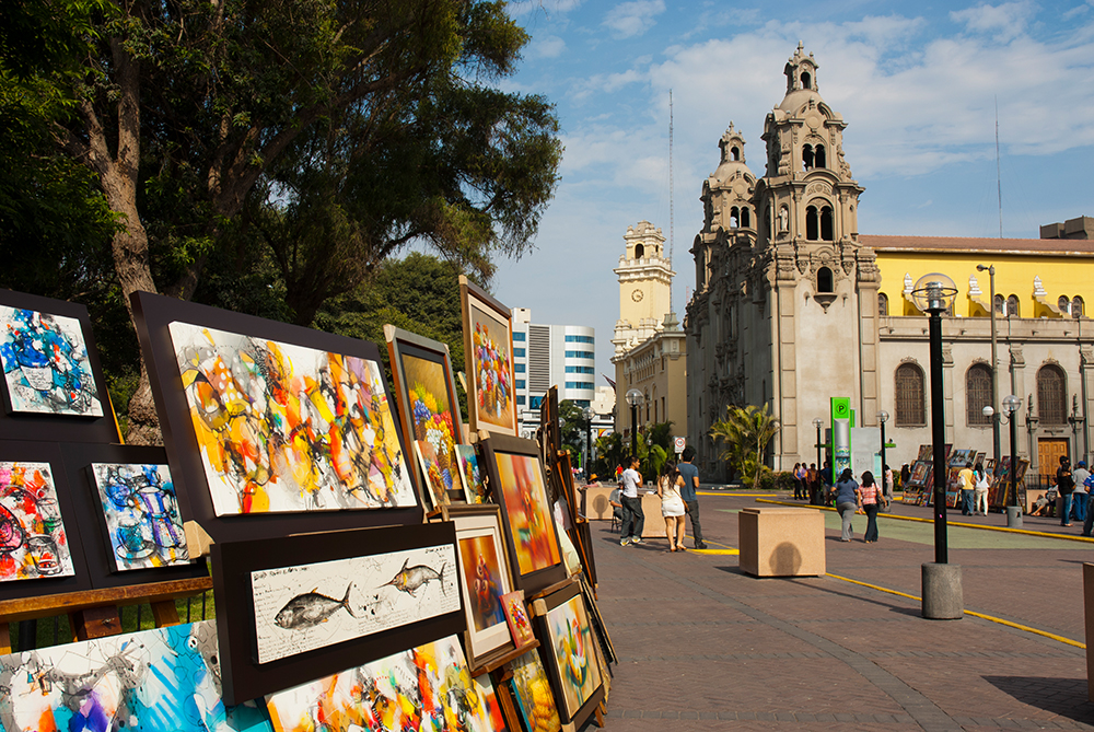 Im Parque Central in Miraflores, Lima, werden Bilder verkauft. Im Hintergrund ist die Kirche "Virgen Milagrosa" zu sehen